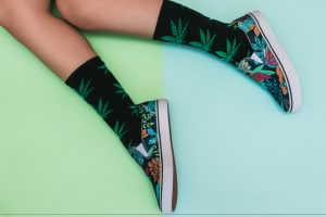 Flat lay fashion set: girl's legs in weed print socks and palm print shoes on pastel backgrounds. Minimal concept. Top view.